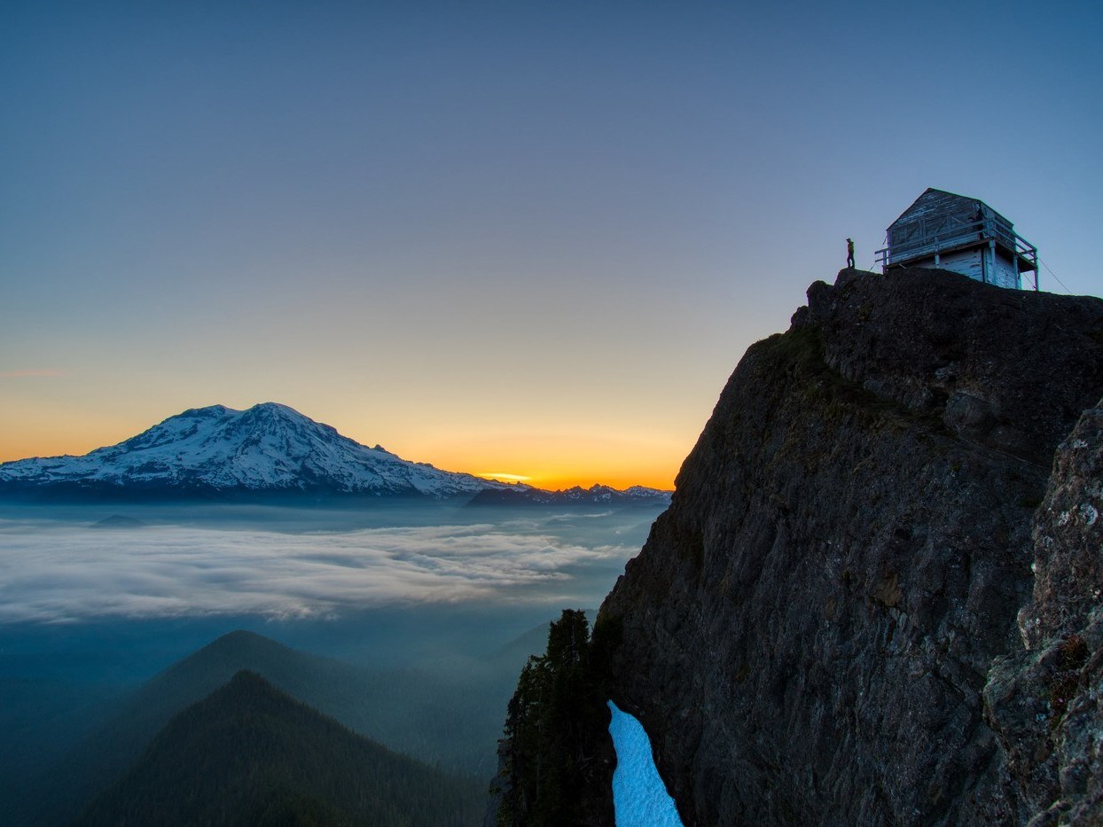 High Rock Lookout perched on a cliff edge at sunset, with Mount Rainier rising above a sea of clouds